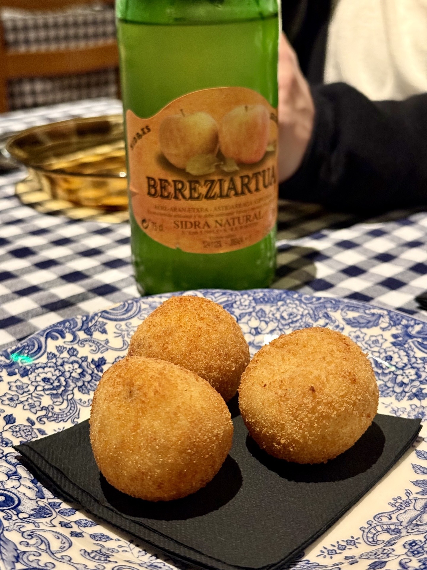 Knusprige hausgemachte Kroketten und eine Flasche baskischer Natur-Sidra auf einem gedeckten Tisch.