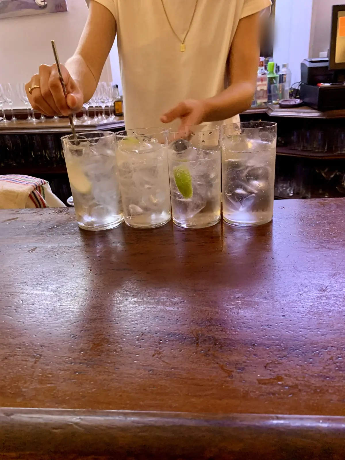 Vier Gin-Tonic mit Limette auf einer dunklen Holztheke, dahinter wird gerade umgerührt – später Abend in einer Bar in Donostia-San Sebastián