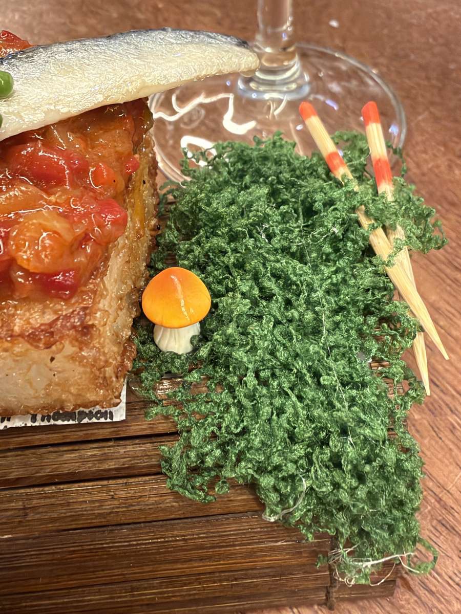 Nahaufnahme des Nigiri Txistulari in der Tatapas Gastroteka Hondarribia: goldbraun frittierter Reisblock mit Piquillo-Tatar und Sardelle, daneben Moos-Dekoration, ein orangefarbener Mini-Pilz und zwei Essstäbchen