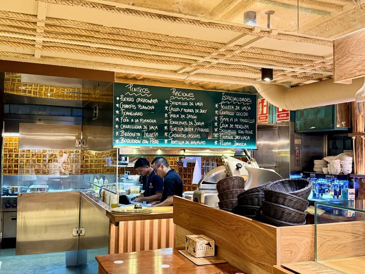 Kreidetafel im Txinparta in Donostia-San Sebastián mit Pintxos wie Puerro carbonara und Txangurro, Raciones und Asador-Spezialitäten wie Txuleta de vaca und Rape a la parrilla, darunter die offene Küche